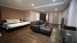 A modern hotel room with a bed, a sofa, a glass coffee table, and a TV. - Platinum Luxury Suite | Modern City Getaway (Bangkok)