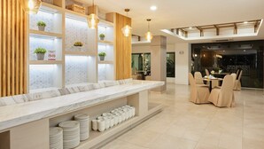 A modern hotel lobby with a marble reception desk, pendant lighting, and a dining area with beige chairs. - Platinum Luxury Suite | Modern City Getaway (Bangkok)