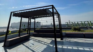 Een terras op het dak met een pergola en een heldere lucht, met in de verte een stadsgezicht.
