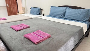 Habitación de hotel con dos camas, cada una con cubrecama gris y toallas rosas. Hay una puerta de madera y una silla en la habitación.