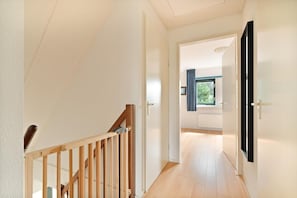 Ein Flur mit einer Holztreppe, einer Tür zu einem Zimmer mit Fenster und einem Heizkörper an der Wand.