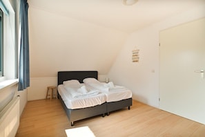 Une chambre avec un lit, un petit tabouret, une porte blanche et un panneau mural.