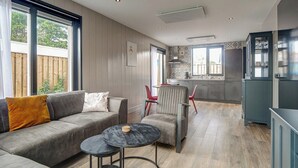 Een moderne woonkamer met een grijze bank, een klein rond tafeltje en een keuken op de achtergrond.