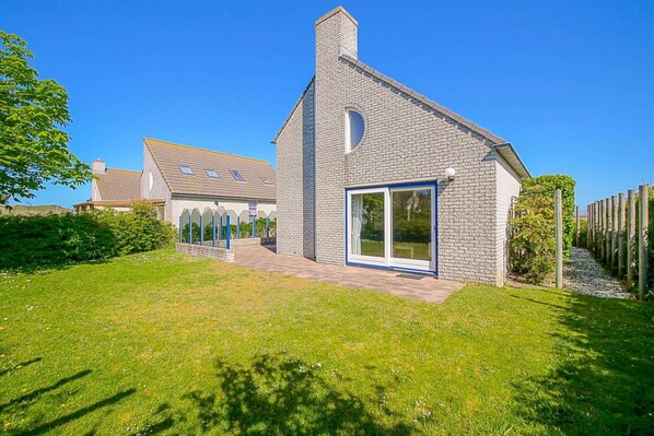 Une maison moderne avec une façade en pierre, de grandes fenêtres et une pelouse bien entretenue.