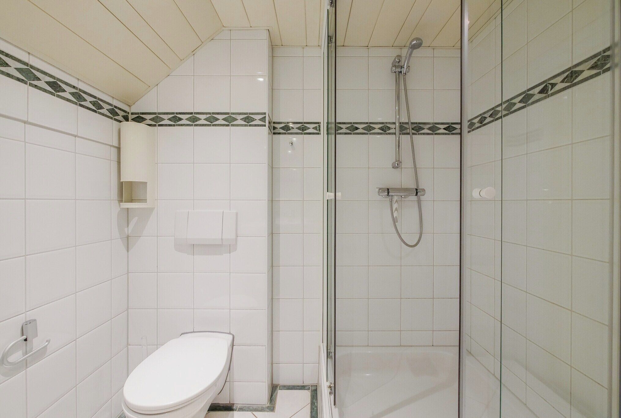 Une salle de bain avec des toilettes, une douche à parois de verre et des murs carrelés.