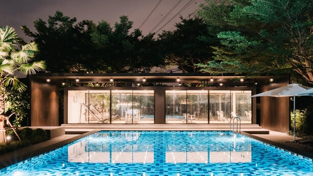 A swimming pool with a tiled floor, surrounded by a building with large glass windows and a covered seating area. - Superior Twin Retreat | Relaxed Stay for Two (Bangkok)
