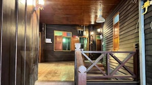 Eine Holztreppe führt zu einer Veranda mit Geländer, einer Holztür und einem Fenster mit grünem Rahmen.