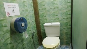A bathroom with green patterned tiles, a toilet, a paper towel dispenser, and a sign instructing to put toilet paper in the bin. - Social Male Dorm | Bed in 8-Bed Friendly Space (Chiang Mai)