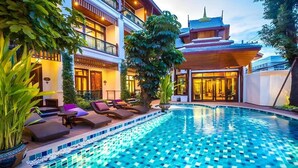 Un hotel con piscina, sillones de descanso y un estilo arquitectónico tradicional.