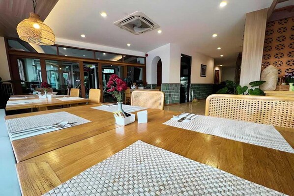 Un restaurant avec des tables en bois, des sets de table en fibres tressées et des chaises en osier.