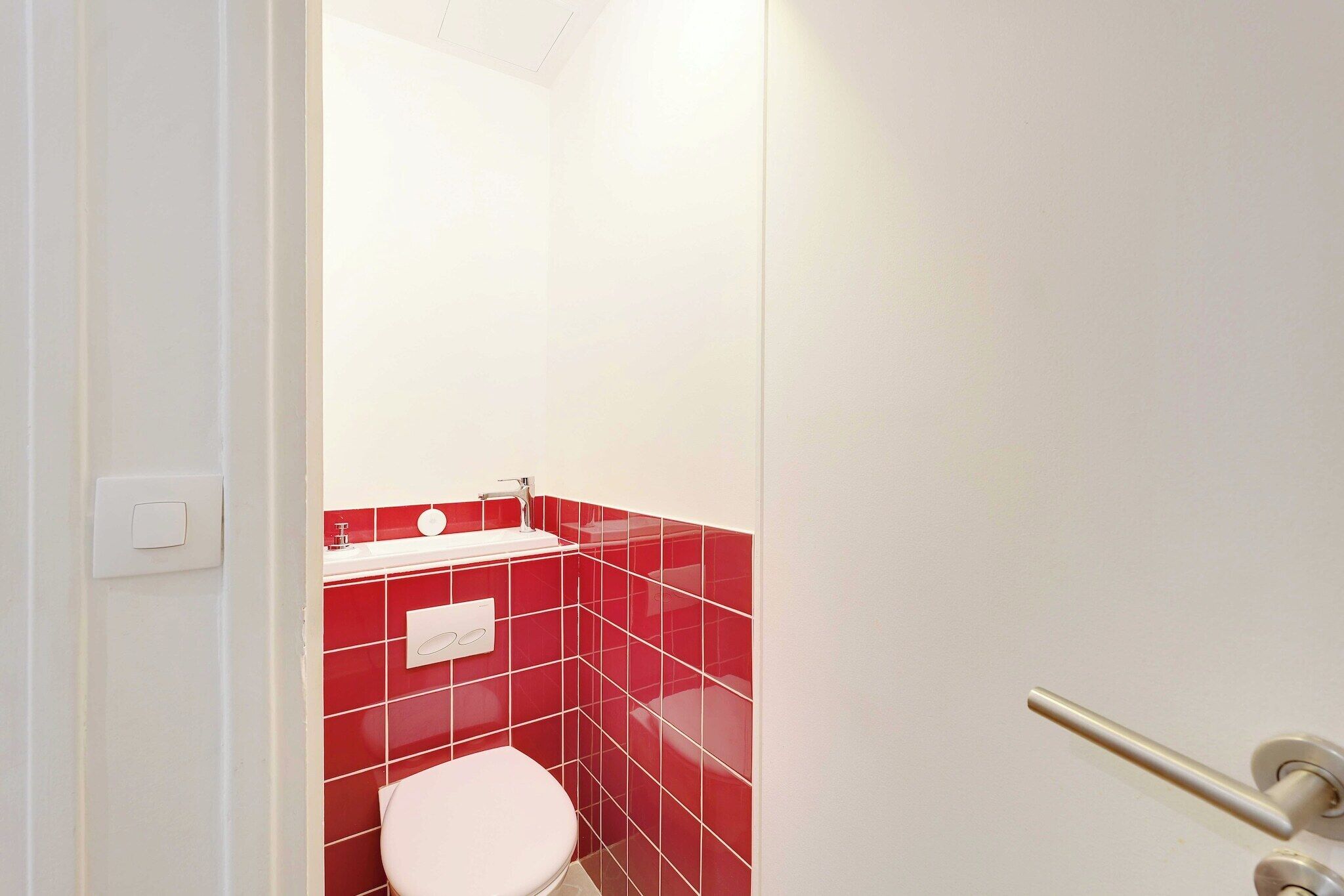 A bathroom with a white toilet, red tiles, and a white sink.