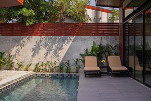 A modern outdoor pool area with two lounge chairs, a small pool, and a wall with climbing plants and a red fence. - Charming 2-Bedroom Family Pool Villa (Pattaya)