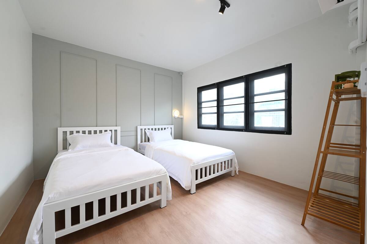 Ein Schlafzimmer mit zwei weißen Betten, einem Fenster mit Jalousien und einer Holzleiter.