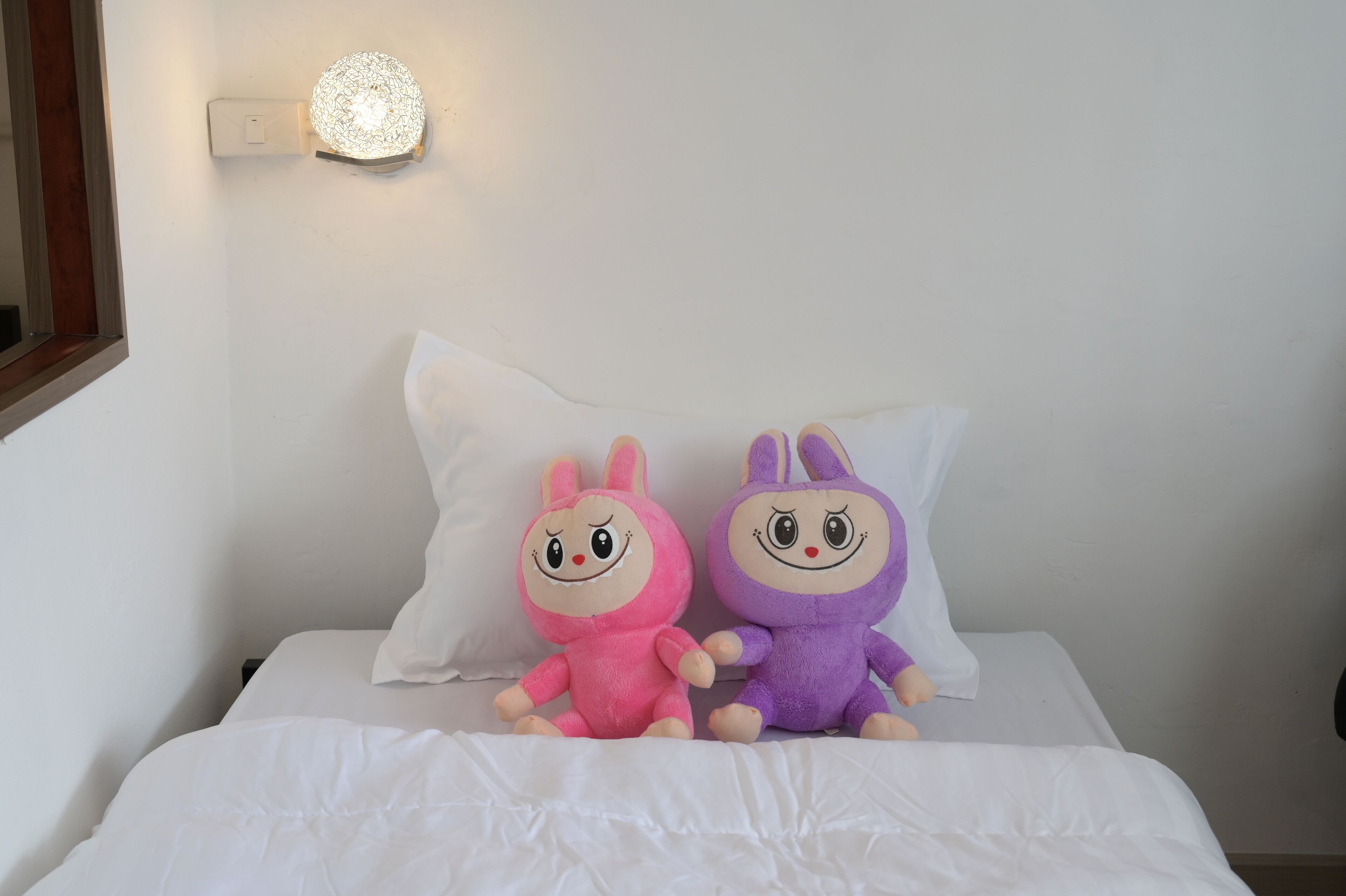 A bed with white bedding and two plush toys on it.