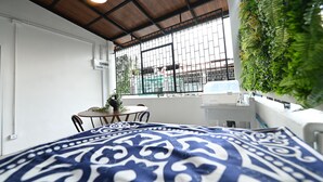 A room with a bed, a window with a view of buildings, a table with chairs, and a potted plant. - La Or Heritage Suites MRT Hua Lamphong (Bangkok)