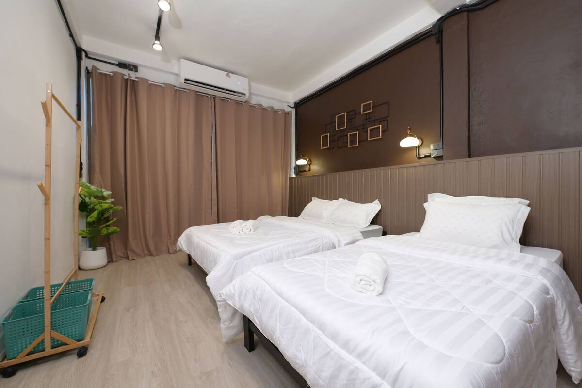 Ein Hotelzimmer mit zwei Betten, einer Zimmerpflanze, einem Rollwagen und einer Wandklimaanlage.