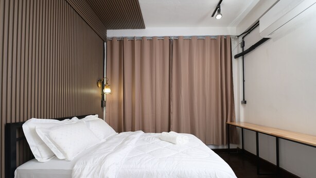 A neatly made bed with white linens, a wooden headboard, and a bedside table with a lamp. - La Or Heritage Suites MRT Hua Lamphong (Bangkok)