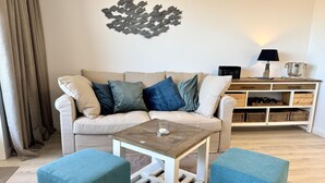 Ein Wohnzimmer mit einem beigefarbenen Sofa, türkisfarbenen Kissen, einem Holztisch als Couchtisch und einem weißen Nachttisch mit Lampe.