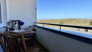 Ein Balkon mit Tisch, Stühlen, einem Metallbehälter und einem Blumenvasen.