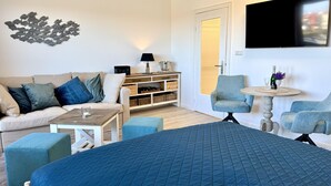 Ein modernes Hotelzimmer mit Bett, Sofa, einem kleinen Tisch, Sessel, Fernseher und einer Wandablage.