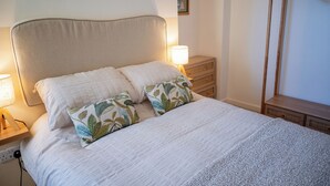 Una cama bien hecha con un cabecero, dos lámparas de noche y una mesita de noche de madera.