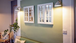 Una habitación con dos ventanas de marco blanco, una pared verde, una silla de madera y un sofá verde.