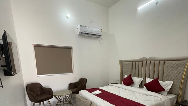 A modern bedroom with a bed, two chairs, a small table, a TV, and an air conditioning unit.