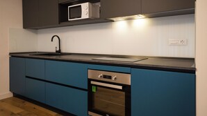 Ett modernt kök med mörkblå skåp, en ugn i rostfritt stål, en mikrovågsugn och en svart diskho.
