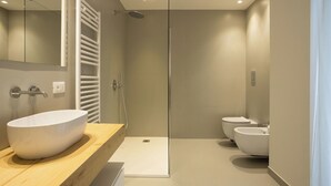 Ett modernt badrum med en stor, vit tvättställ, en dusch med glasväggar och två toaletter.
