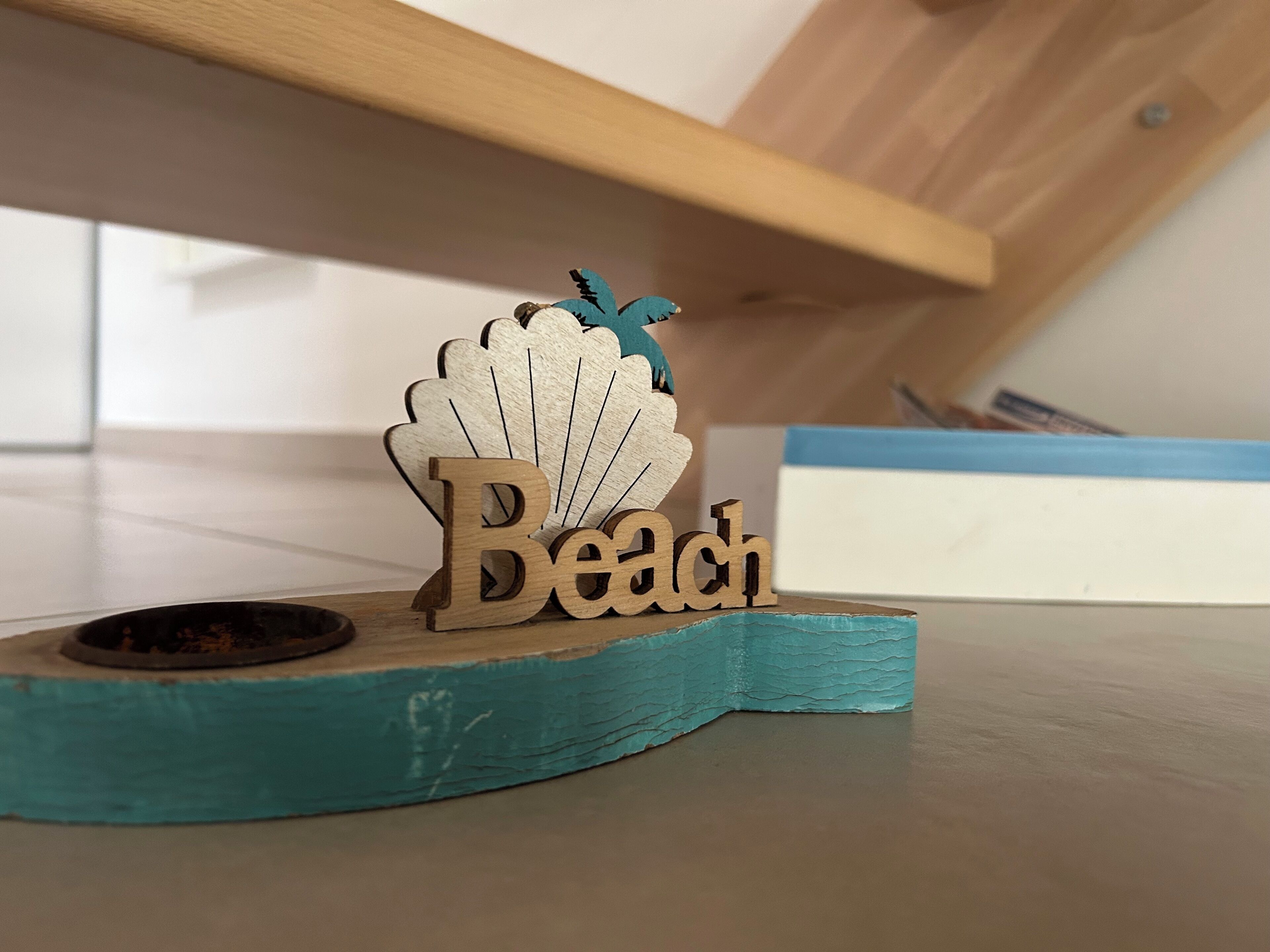 Una placa de madera con la palabra 'Beach' y un diseño decorativo de concha.