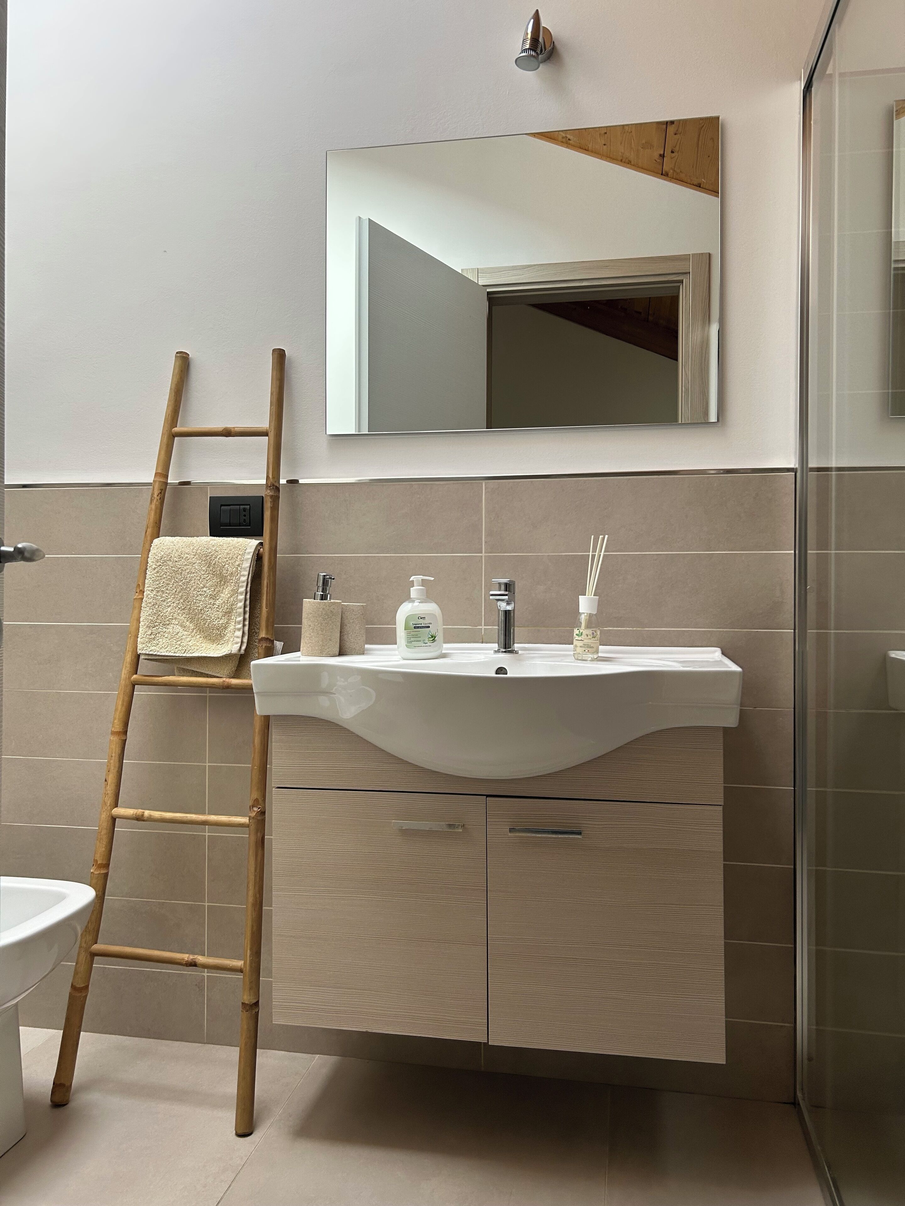 Un baño con un lavabo blanco, espejo y una escalera de bambú.