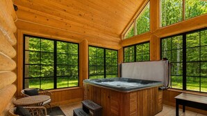 A wooden cabin interior with a hot tub, wicker furniture, and large windows offering a forest view. - Fiddler Lake Resort - Rabbit 24 (Mille-Isles)