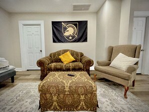 A living room with a patterned ottoman, two armchairs, and a wall-mounted flag. - Walk to West Point USMA - Marvelous 4 Bedroom house in Highland Falls -Sleeps 12 (Highland Falls)