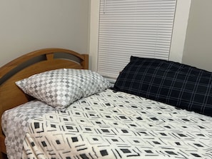 A bed with a geometric patterned bedspread, two pillows with checkered and plaid designs, and a wooden headboard. - Walk to West Point USMA - Marvelous 4 Bedroom house in Highland Falls -Sleeps 12 (Highland Falls)