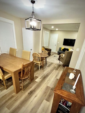 A dining area with a wooden table and chairs, a chandelier, and a living room with a sofa and television. - Walk to West Point USMA - Marvelous 4 Bedroom house in Highland Falls -Sleeps 12 (Highland Falls)