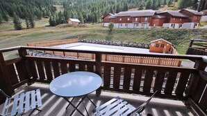 A balcony with a table and chairs, overlooking a mountainous area with buildings and a forest. - Dba205 - 1 Bedroom Apartment + Sleeping Alcove - Balcony - Sleeps 6 - 1800 Area (Puy-Saint-Vincent)