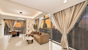 Ein modernes Wohnzimmer mit einer großen Couch, einem Esstisch und Blick auf die Stadt durch große Fenster.