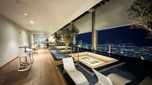 Ein moderner Lounge-Bereich mit Blick auf die Stadt, ausgestattet mit einem langen Tisch und Sitzgelegenheiten sowie einem kleinen Innenhofgarten.