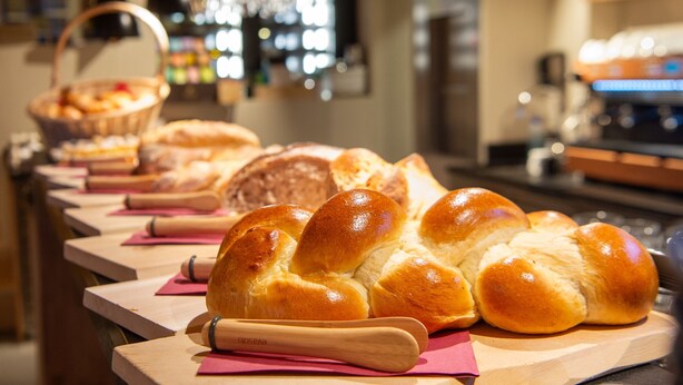 Une vitrine de boulangerie présentant diverses sortes de pains et de viennoiseries, un rouleau à pâtisserie et un panier de pain.