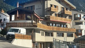 Un hôtel à plusieurs étages, doté de balcons, sur lequel on peut lire l’inscription « Aurora », avec une chaîne de montagnes en arrière-plan.