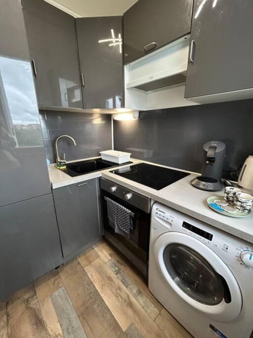 Une cuisine compacte avec des meubles gris, un four encastré, un évier et un lave-linge.
