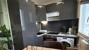 Kompakti keittiö, jossa on tummat kaapit, puinen työtaso ja sisäänrakennettu pesukone.