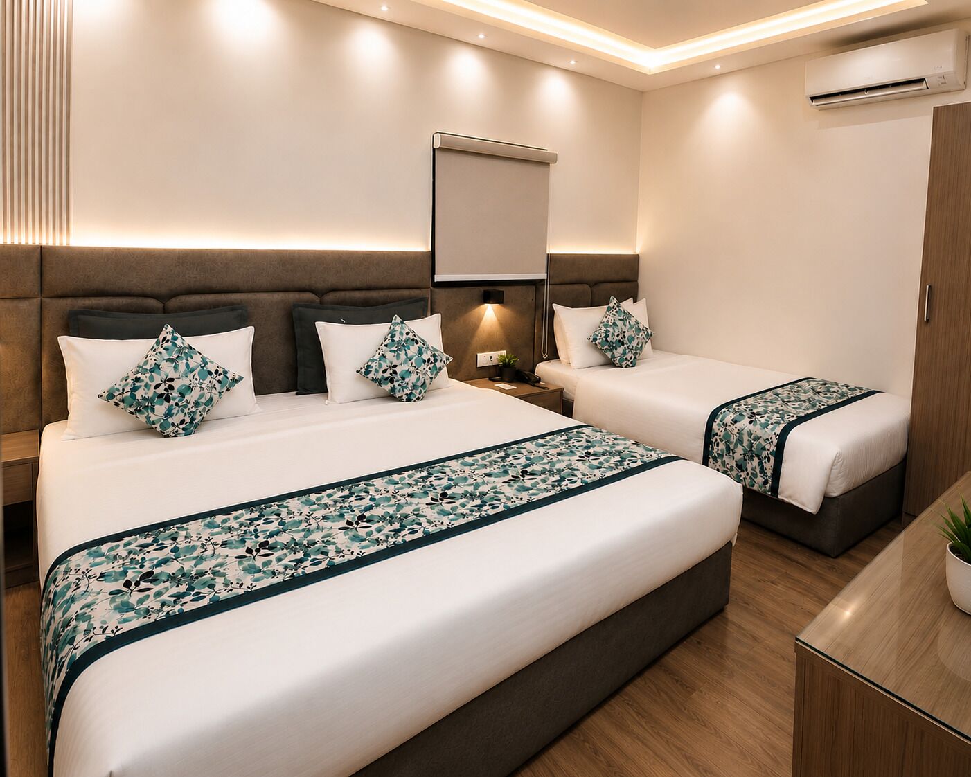 A hotel room with two beds, a bedside table, a nightstand, a mirror, and an air conditioning unit.