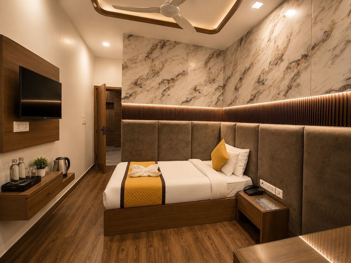 A modern hotel room with a large bed, a flat-screen TV, a bedside table, and a marble-patterned wall.