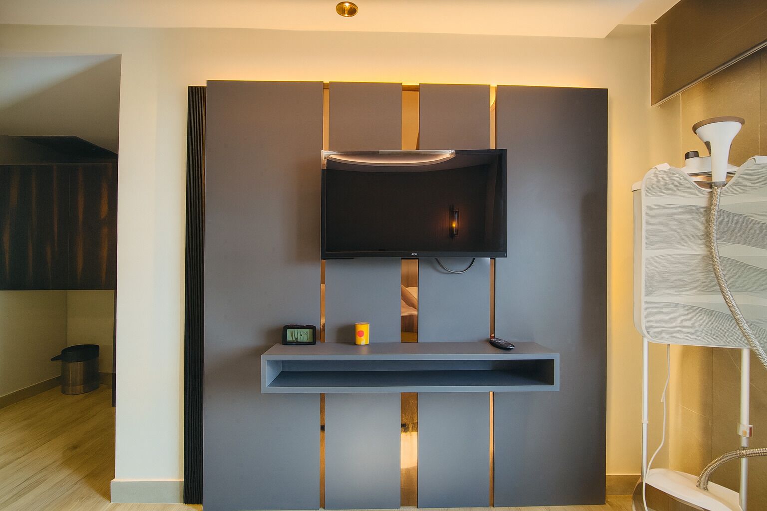 Una sala de estar moderna con un televisor de pantalla plana montado en una pared, un estante pequeño debajo y una tira de luces decorativa.