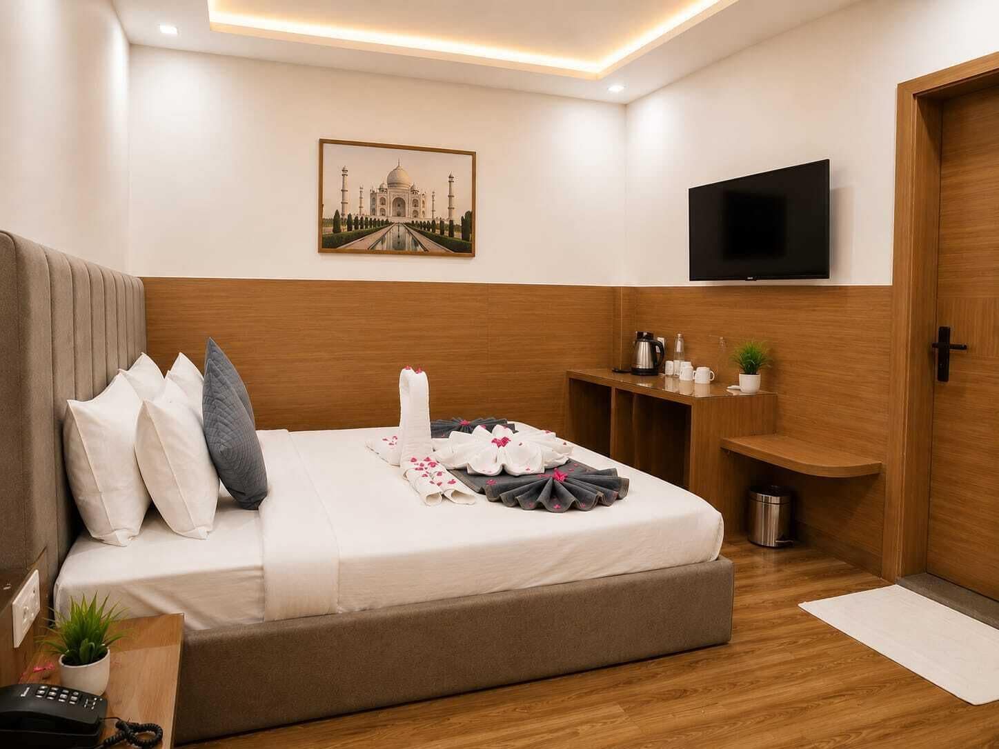 A hotel room with a bed, a television, a painting of the Taj Mahal, a coffee maker, and a small plant.