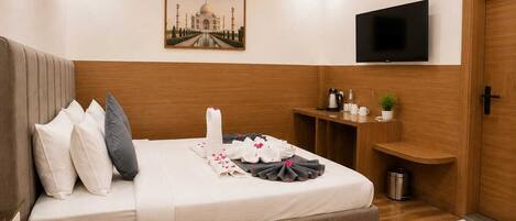 A hotel room with a bed, a television, a painting of the Taj Mahal, a coffee maker, and a small plant.