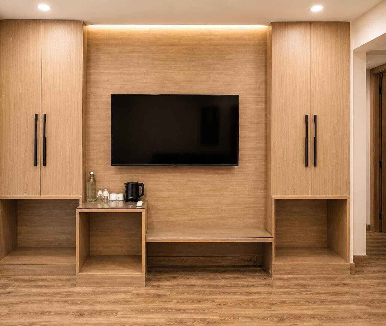 Une chambre moderne dotée d’un téléviseur à écran plat fixé au mur, de meubles en bois et d’une petite table sur laquelle se trouve une machine à café.