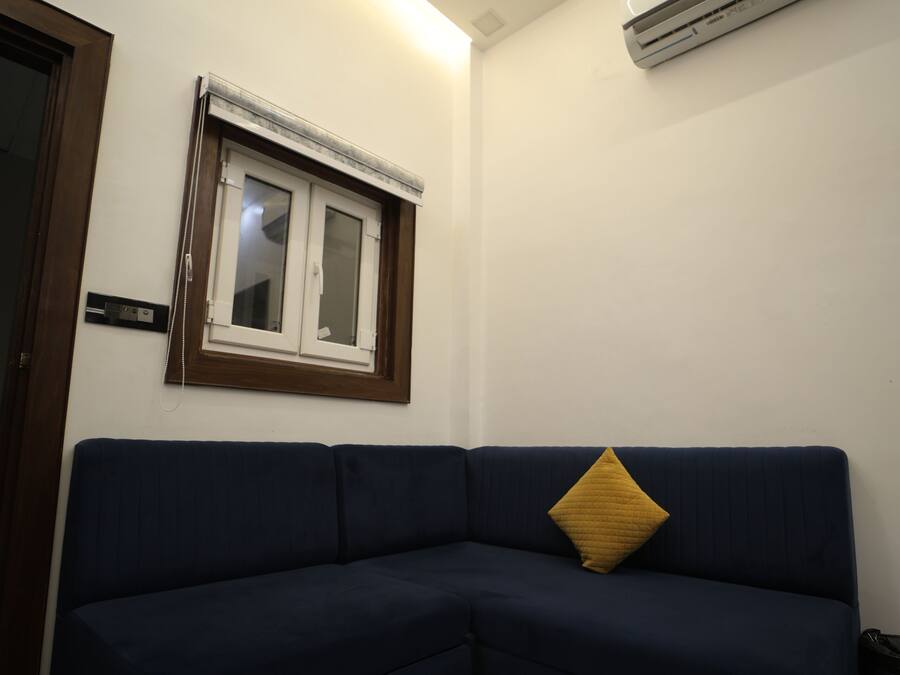 Un canapé bleu foncé avec un coussin jaune, une fenêtre avec des stores et un appareil de climatisation fixé au mur.