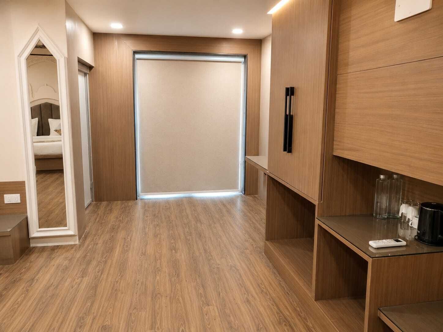 A hotel room with a wooden floor, a bed, a wardrobe, and a small table with a remote control.